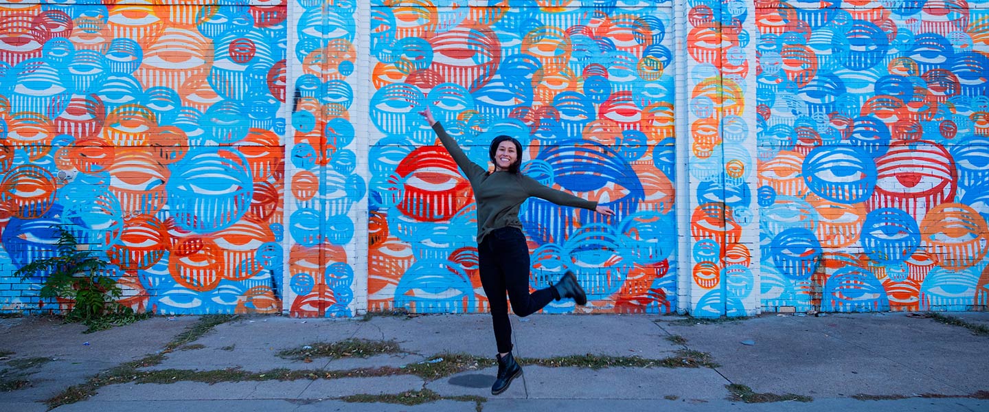 woman jumps in front of colorful mural