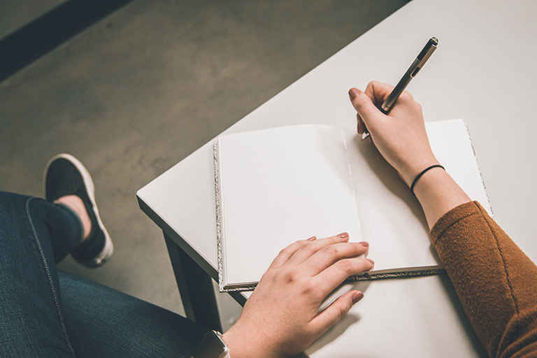 hands hold a pencil and write on a notebook desk