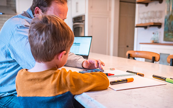 man and toddler look at phone while seated at kitchen counter strewn with markers and paper