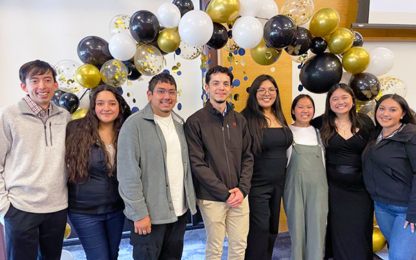 a group of 1LEADS first-gen students poses for a photo beneath a blue and gold balloon arch