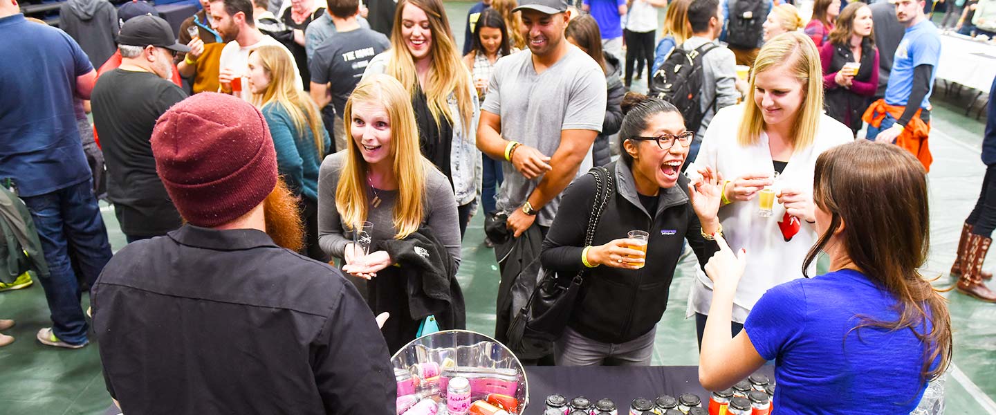 a large crowd gathers in the Regis Fieldhouse while attendees enjoy beers and chat with brewers pouring beers