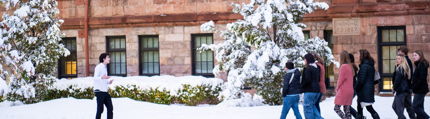 Regis affiliated person leads group on tour in front of main hall. Snow covers the ground