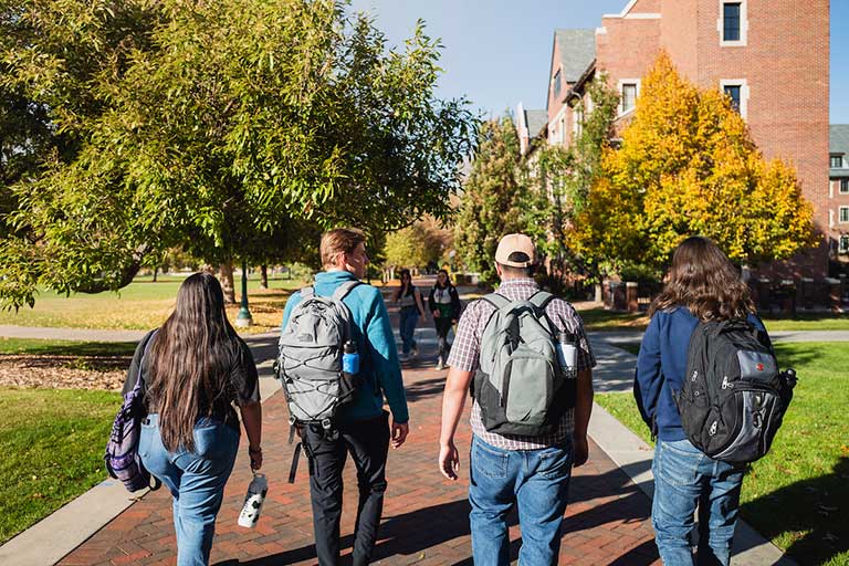 a group of students wearing backpacks walks along the quad on the Regis campus