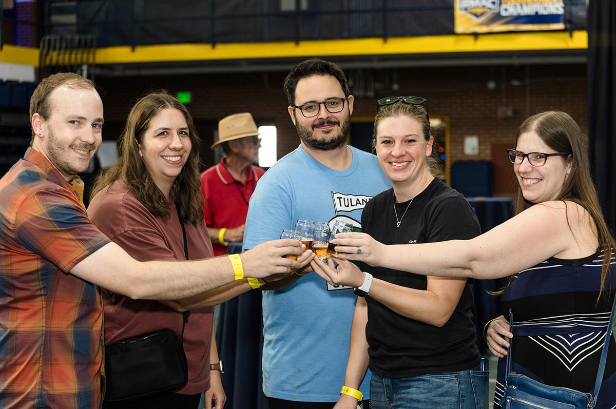 a group of five attendees raise their glasses in a toast during Iggy Beerfest in the fieldhouse during blue and gold weekend on the Regis campus