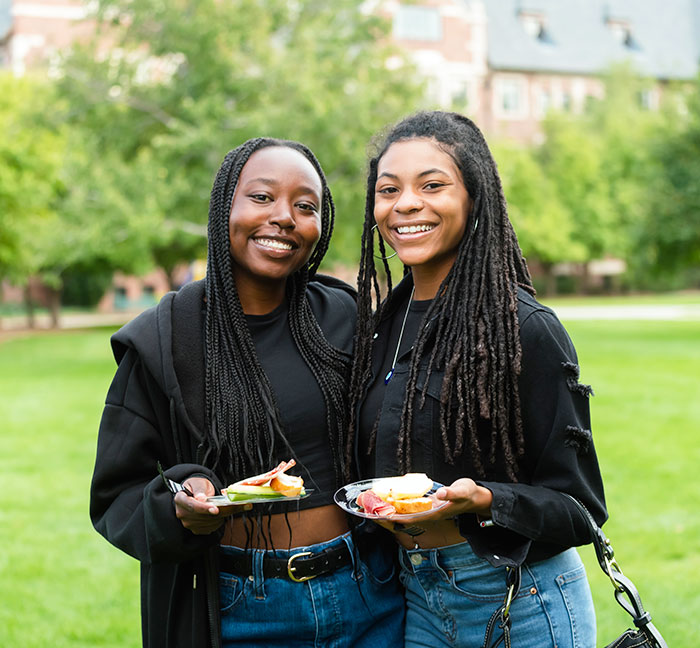 Two students smile and pose for a photo while enjoying refreshments on the quad at Blue & Gold Weekend