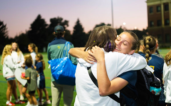 a student and parent embrace at the end of a Lacrosse match on the Match pitch field during blue and gold weekend on the northwest Denver campus