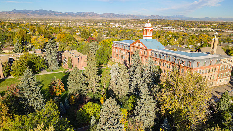 aerial photo of the Regis campus showing Main Hall, West Hall, the Chapel and the Rocky Mountains in the background.