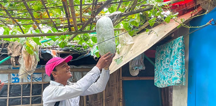 A man holds a large gourd near the leaf lined roof of a bamboo structure in Myanmar