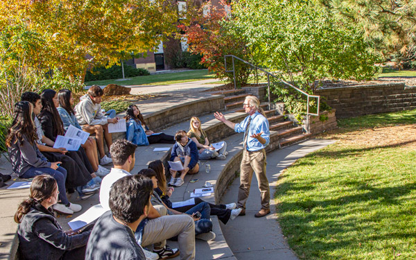 professor speaking to a group of students seated outside on campus on a sunny day