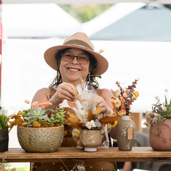 a vendor smiles while arranging flowers she is selling in her tent at horseshoe market