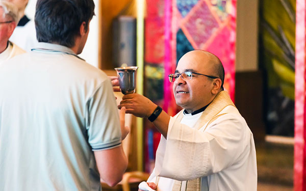 a priest offers a cup to a congregant during mass in the Chapel on the Regis campus