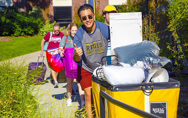 a current regis student wheels a cart of belongings for a new student as parents follow during move-in day on the northwest denver campus