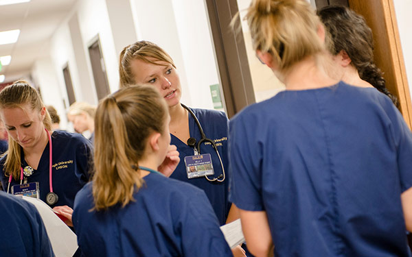 nursing students wearing scrubs gather for discussion outside Regis nursing sim lab