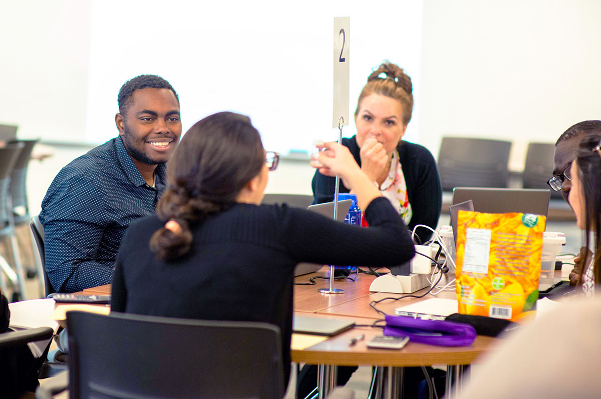 pharmacy students sit around a table and discuss during a TBL session on the Regis campus