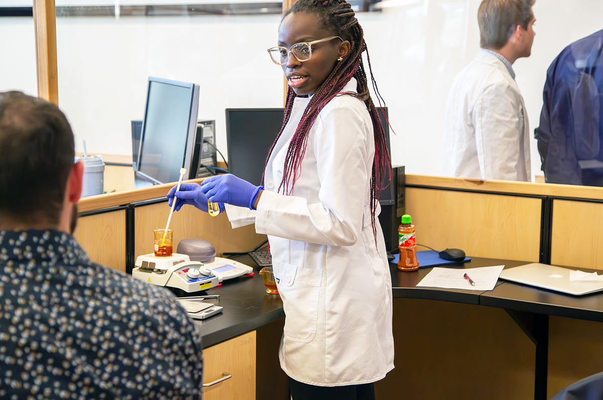 a pharmacy student talks to her lab partner as she measures a liquid in a beaker in the pharmacy lab on the Regis campus