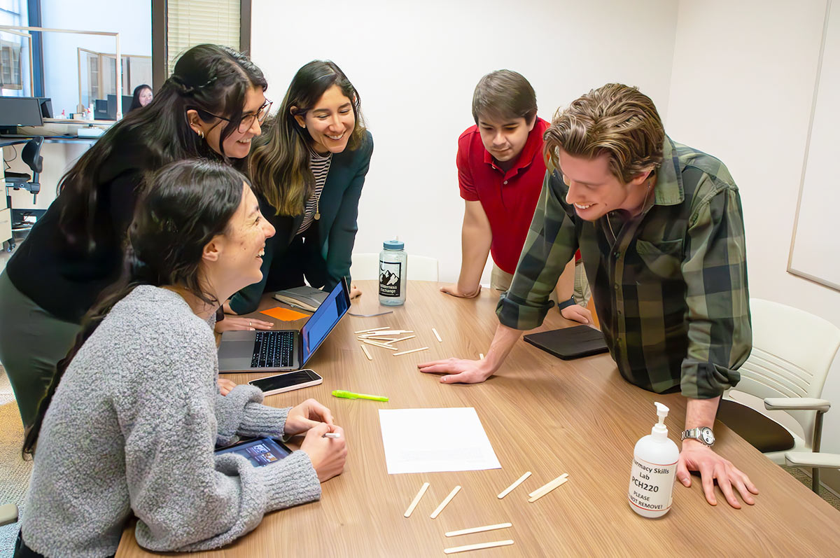 a group of students gathered around a table with scattered supplies smile and talk