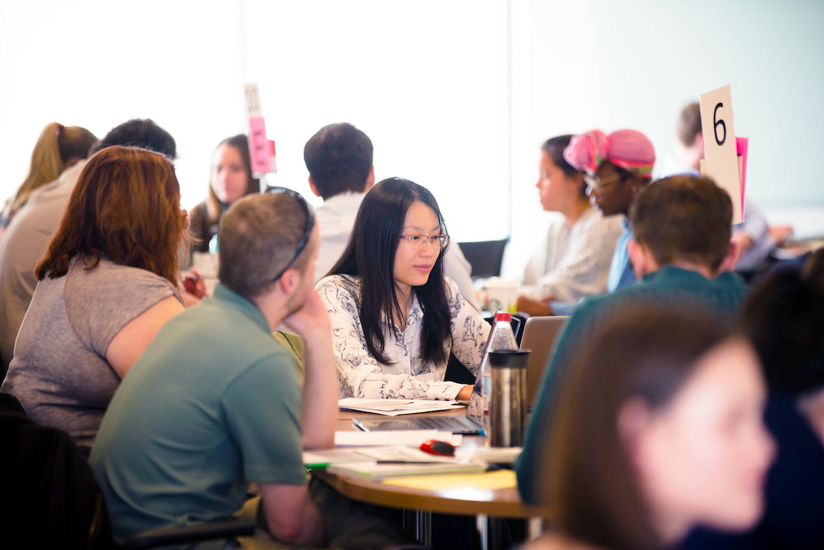 several groups of pharmacy students sit around tables and work during a TBL session on the Regis campus