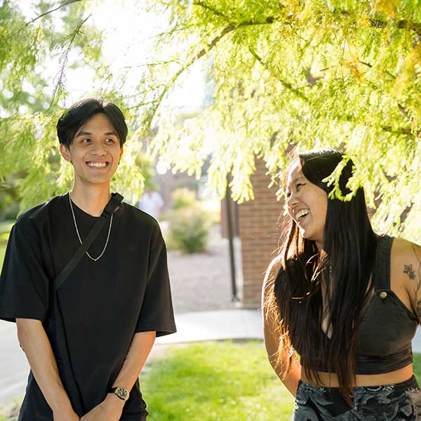 two regis students stand together smiling and laughing on the quad