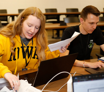 two participants seated together, one sorting through papers and the other working on laptop