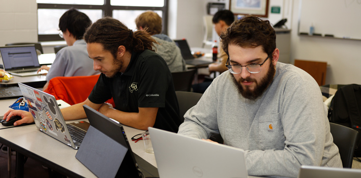 two focused participants seated together working on multiple laptops