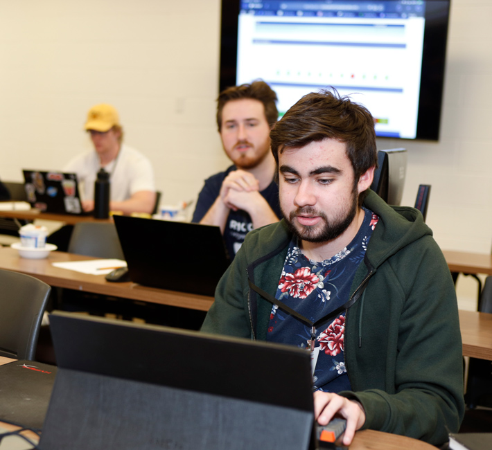 participant talking and working on laptop while teammates overlook