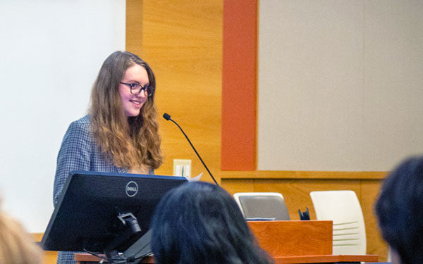 Person up front speaking in front of a podium in front of a crowd of people at tables