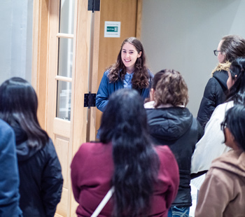 Group of people stand around Regis affiliate giving them a tour of campus indoors