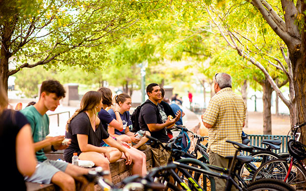students sit on a wall near a bike rack in a downtown park 