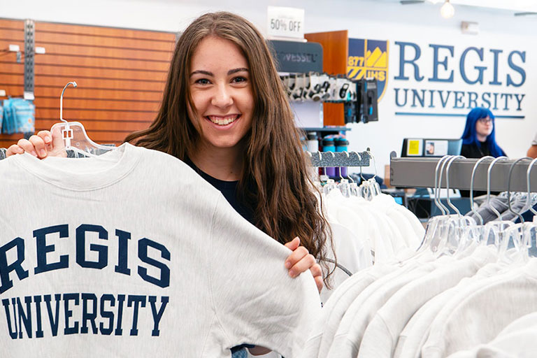 a student holds up a Regis sweatshirt in the Ranger Station bookstore on the Northwest Denver Campus