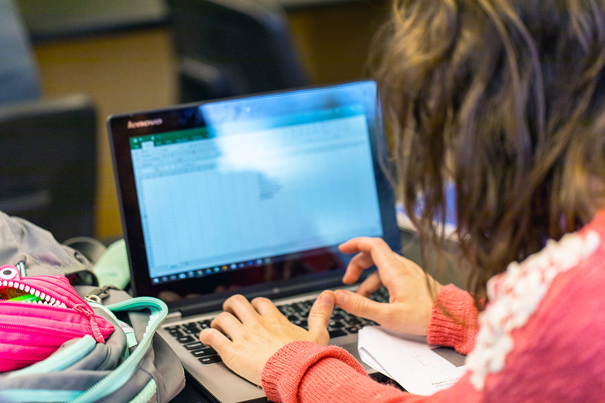 A Regis University student using a laptop in class, focused on their studies with notebooks and books on the desk.