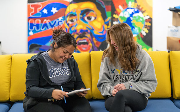 two students sit on a sofa while studying on the Regis campus