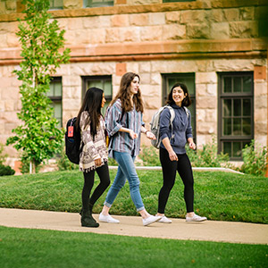 3 students with backpacks on walking in front of Main Hall together