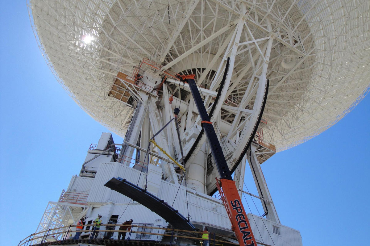 A crane lifting a runner segment that is part of major surgery on a giant, 70-meter-wide antenna