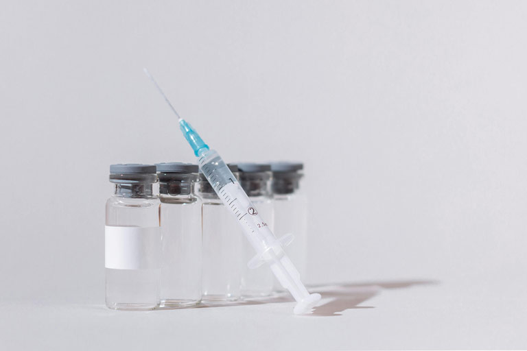 Syringe or injection needle with a blue-tipped plunger positioned alongside several small glass vials.