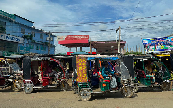 four small, colorful golf-cart-like vehicles drive down a street in Myanmar