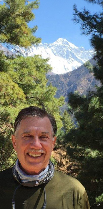 Roger stands in front of pine trees and the mountains