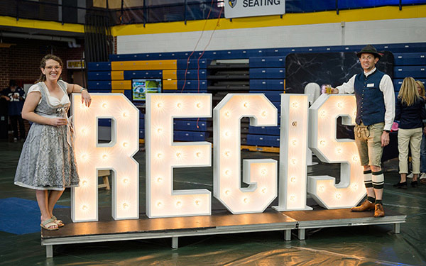 Big Regis Sign in white in the middle of two people leaning against it on either side