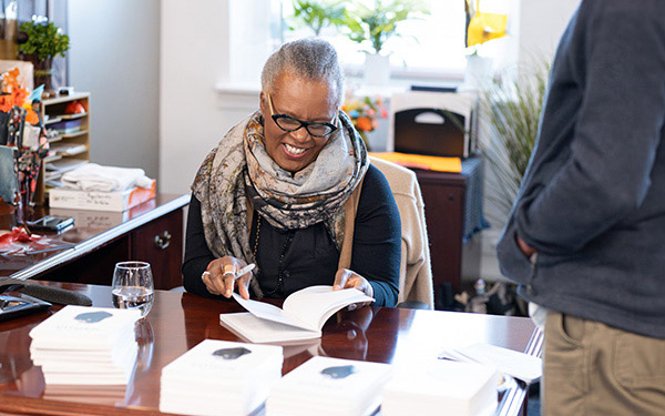 Claudia Rankine sits down at a desk while looking down at an open book she has in her hand