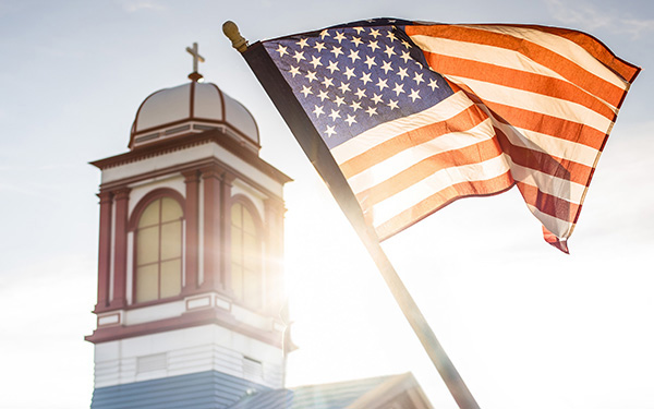 An American flag waves in the wind with Regis' Main Hall in the background