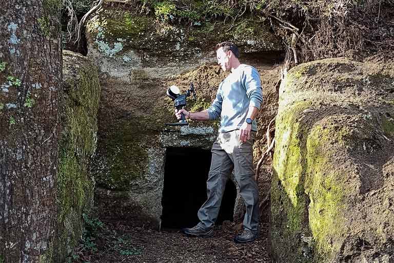 Man in a trench holds equipment in hand while looking down at it