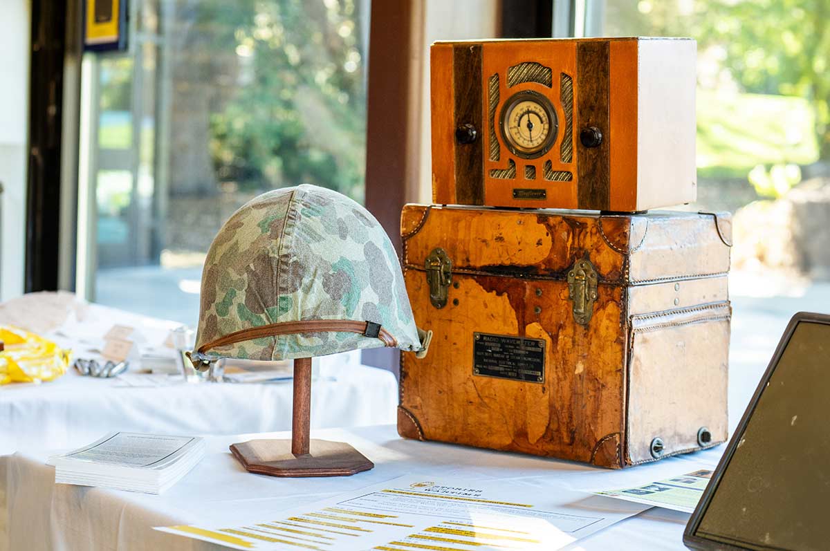 Military Helmet on a stand. Both are on a table with a white sheet over it. To its right is a box and on top is a vintage radio