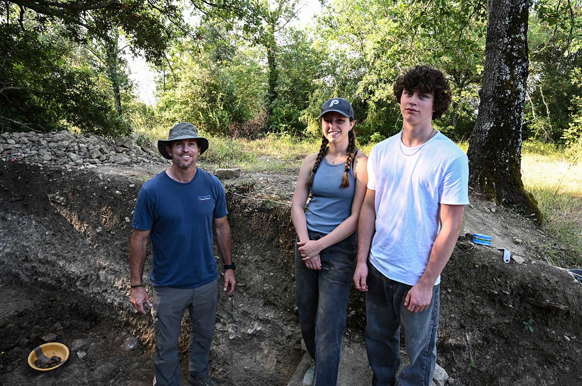 Brad lidge stands with a young woman and young man amid diggings in the forest