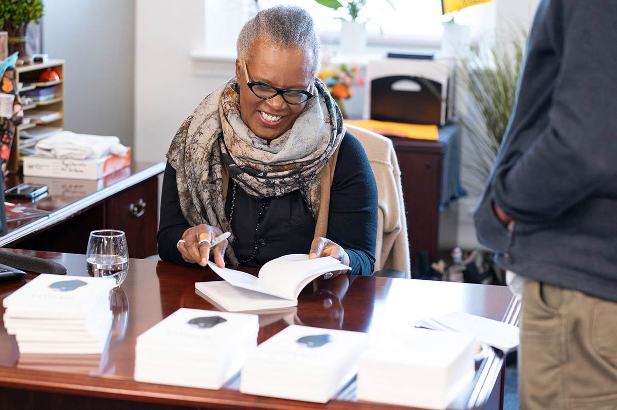 Claudia Rankine sits at a desk signing a copy of her book for a fan who stands nearby waiting