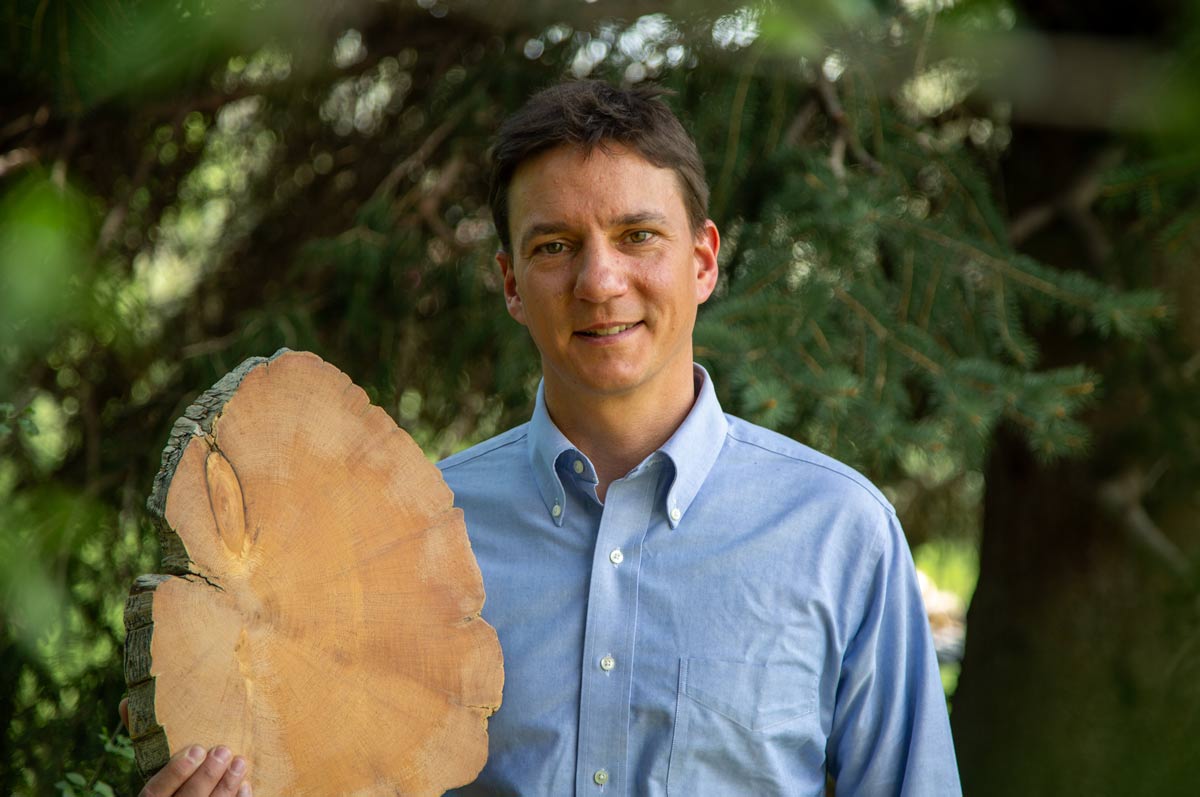 Prof. John Sakulich smiles while holding a tree stump in his right hand