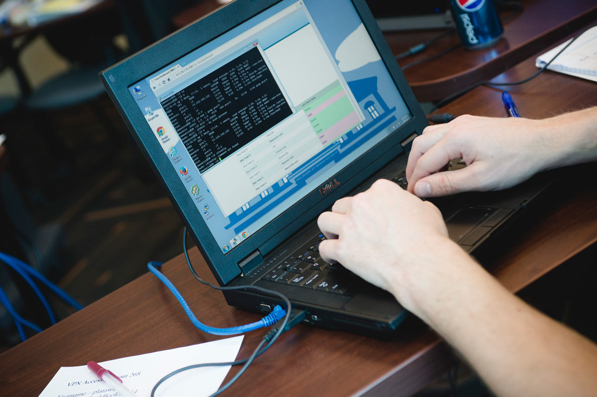 A close up view of a student typing on a laptop with a command-line interface open on the screen.