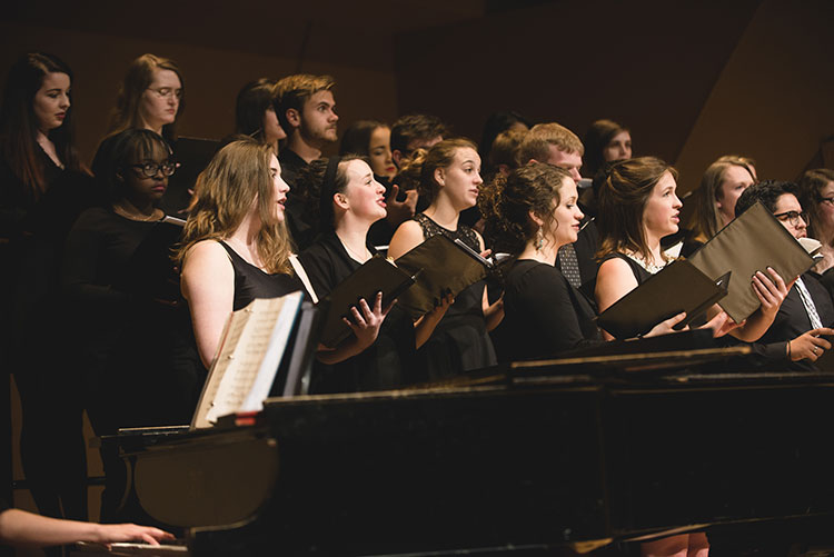 members of the University choir stand on stage and sing during a performance in the Claver Recital Hall on the Northwest Denver Campus