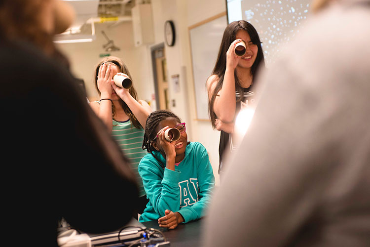 girls in a classroom look through cardboard tubes